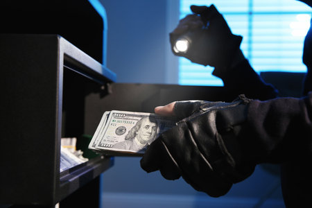 Thief taking money out of steel safe indoors at night, closeup
