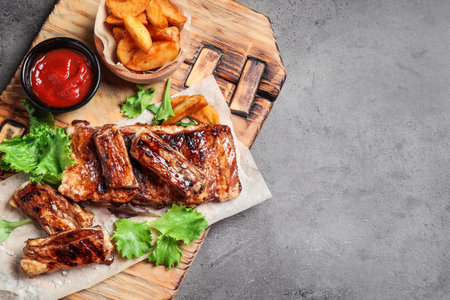 Delicious grilled ribs and garnish on gray table, top view. Space for textの写真素材