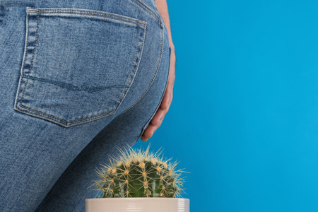 Man sitting down on cactus against light blue background, space for text. Hemorrhoid conceptの写真素材