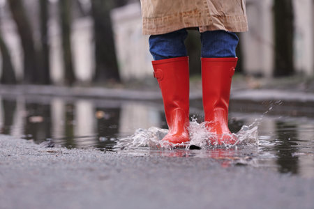 Woman in rubber boots jumping over puddle on rainy day, closeup. Space for textの写真素材
