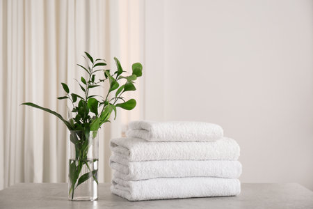Fresh towels and green branches on light gray stone table in bathroomの写真素材