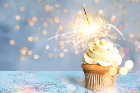 Delicious birthday cupcake with sparkler on blue table against blurred lights. Space for textの写真素材