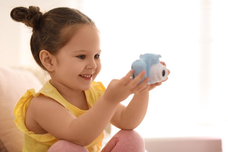 Little photographer taking picture with toy camera on sofa at home