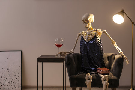 Skeleton in dress with wine sitting at table indoorsの写真素材