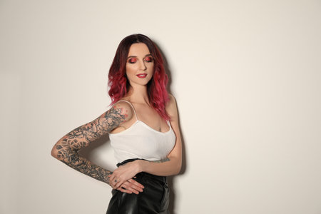 Beautiful woman with tattoos on arms against light background. Space for textの写真素材