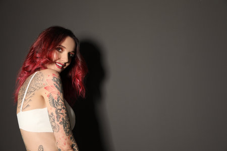 Beautiful woman with tattoos on body against black background. Space for textの写真素材