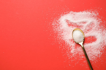 Granulated sugar and spoon on red background, flat lay. Space for textの写真素材