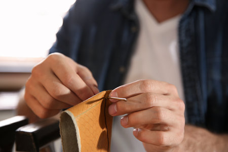 Man sewing piece of leather in workshop, closeup