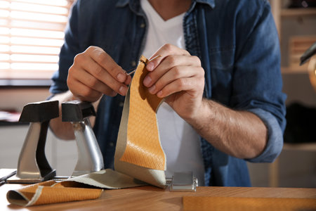 Man sewing piece of leather in workshop, closeup