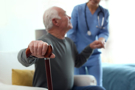 Care worker helping elderly man in geriatric hospice, focus on hand with stick