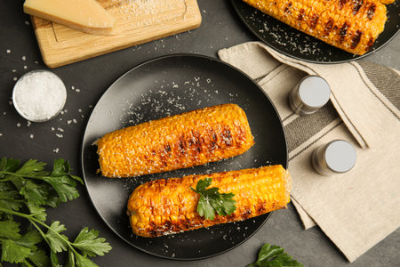Delicious grilled corn cobs on black table, flat lay