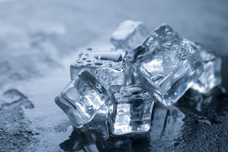 Crystal clear ice cubes with water drops on gray table, closeup