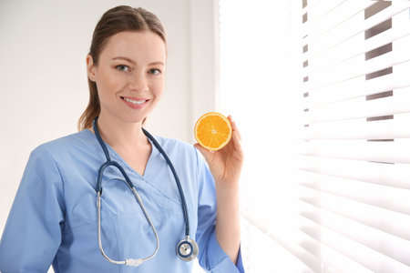 Nutritionist with orange near window in officeの写真素材