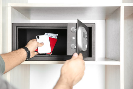 Man putting smartphone, passport and money into steel safe, closeup