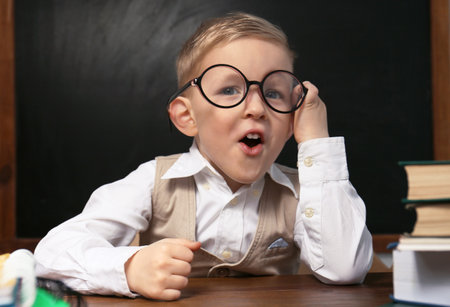 Cute little child wearing glasses at desk in classroom. First time at school