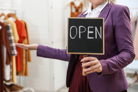 Female business owner holding OPEN sign in boutique, closeup