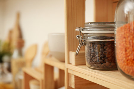 Glass jar with coffee beans on wooden shelf in kitchen, space for textの写真素材