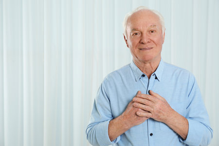Grateful senior man with hands on chest against light background. Space for textの写真素材