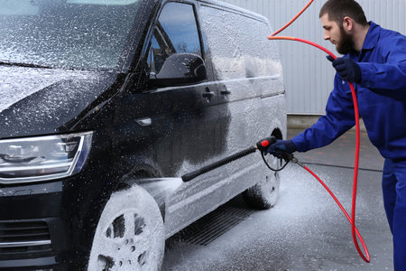 Worker covering automobile with foam at car washの写真素材