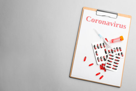 Clipboard with word CORONAVIRUS, test tube, syringe and medicine on light gray background, top view. Space for textの写真素材