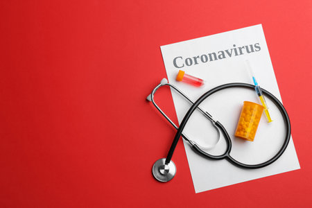 Flat lay composition with word CORONAVIRUS, stethoscope and medicine on red background. Space for textの写真素材