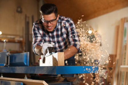 Professional carpenter grinding wooden board with jack plane in workshop, focus on plankの写真素材