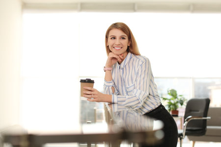 Young businesswoman with cup of coffee relaxing in office during breakの写真素材