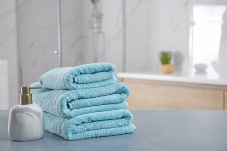 Stack of clean towels and soap dispenser on gray stone table in bathroom. Space for text