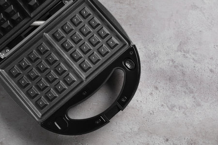 Modern waffle iron on gray stone table, top view