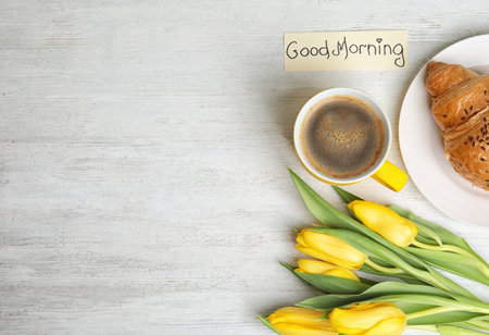 Delicious coffee, croissant, beautiful flowers and card with GOOD MORNING wish on white wooden table, flat lay. Space for textの写真素材