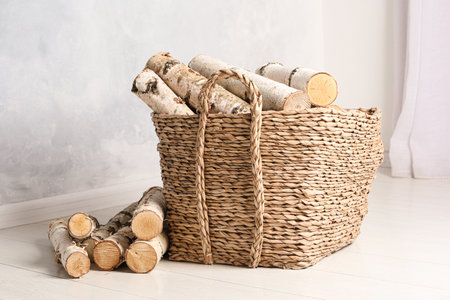Wicker basket with cut firewood on white floor indoorsの写真素材