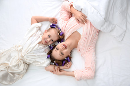 Happy mother and daughter with curlers lying on bed, top viewの写真素材