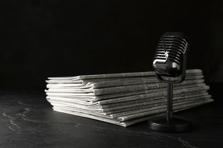 Newspapers and vintage microphone on dark stone table. Journalist's workの写真素材