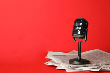 Newspapers and vintage microphone on red background, space for text. Journalist's workの写真素材