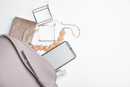 Stylish woman's bag with smartphone and accessories on white background, flat lay. Space for textの写真素材