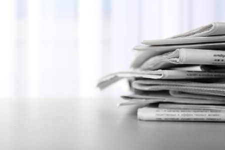 Pile of newspapers on gray table, space for text. Journalist's work