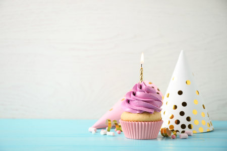 Delicious birthday cupcake with burning candle on light blue wooden table. Space for textの写真素材