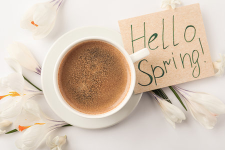 Card with words HELLO SPRING, cup of coffee and fresh flowers on white background, flat layの写真素材