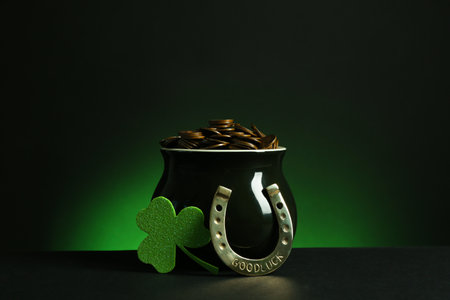 Pot with gold coins, horseshoe and clover on table against dark background. St. Patrick's Dayの写真素材