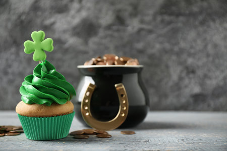 Decorated cupcake and pot with gold coins on gray wooden table, space for text. St. Patrick's Day celebrationの写真素材