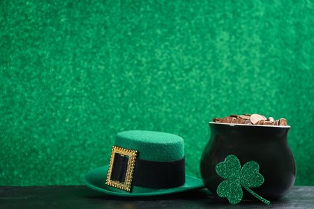 Pot of gold coins, hat and clover on black stone table against green background, space for text. St. Patrick's Day celebrationの写真素材