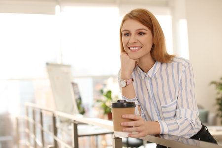 Young businesswoman with cup of coffee relaxing in office during breakの写真素材