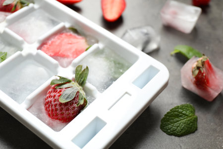 Ice cubes with berries in tray on gray table, closeupの写真素材