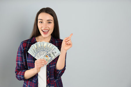 Emotional young woman with money on light gray background. Space for text