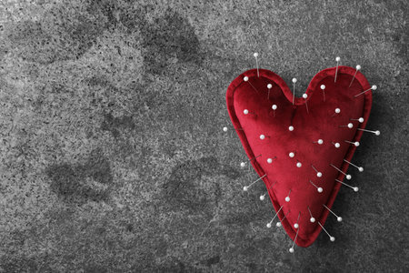 Top view of heart shaped cushion with sewing pins on gray stone background, space for text. Relationship problems conceptの写真素材