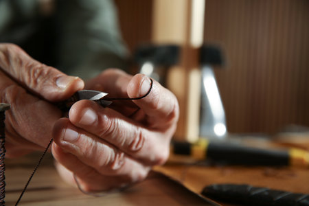 Man cutting thread while working with leather at table, closeup