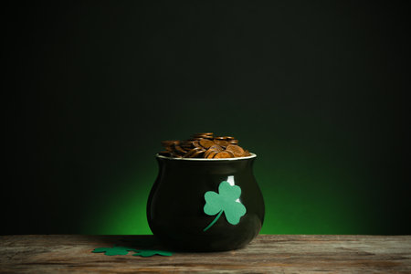 Pot with gold coins and clover on wooden table against dark background. St. Patrick's Dayの写真素材
