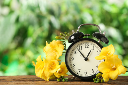 Alarm clock and beautiful spring flowers on wooden table. time change conceptの写真素材