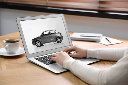 Woman using laptop to buy car at wooden table indoors, closeupの写真素材