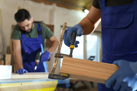 Professional carpenter with wooden board and clamp in workshop, closeupの写真素材